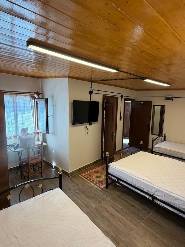 Una habitación con dos camas, un escritorio, un televisor y una ventana con cortinas.