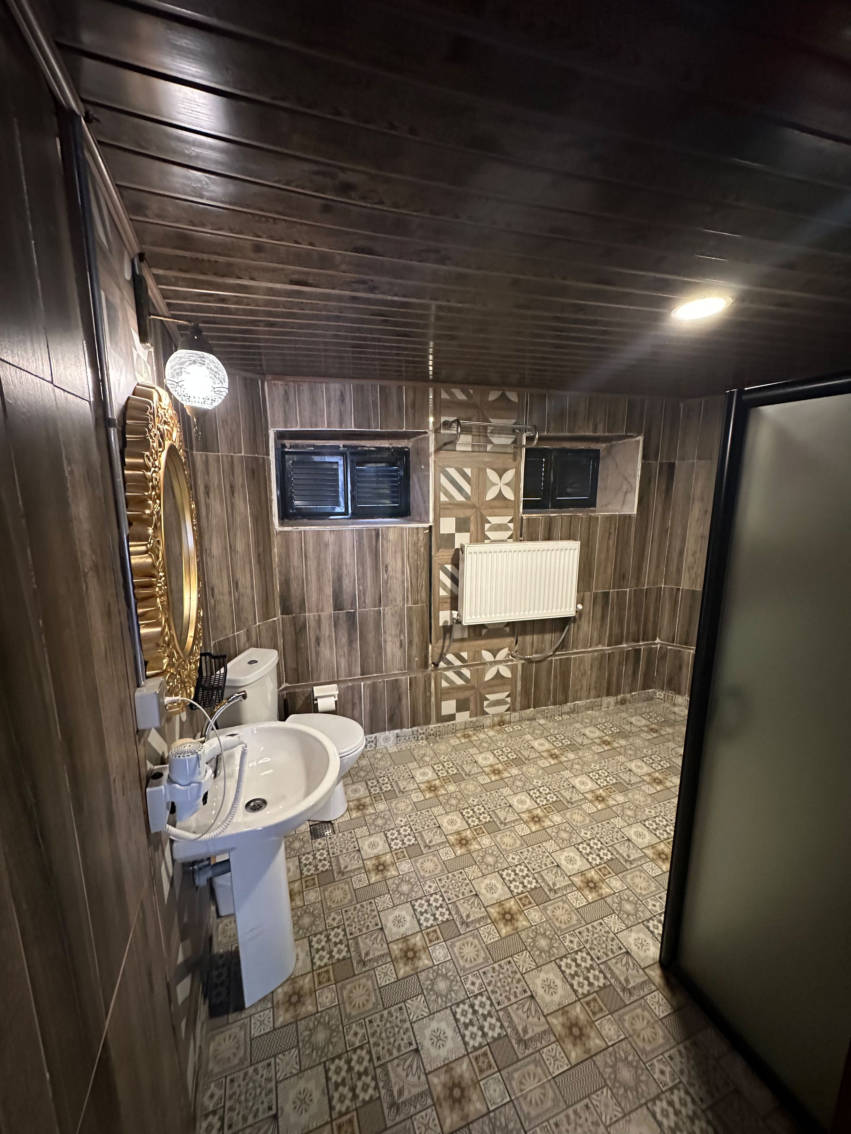 A bathroom with a wooden wall, a sink, a toilet, and a mirror.