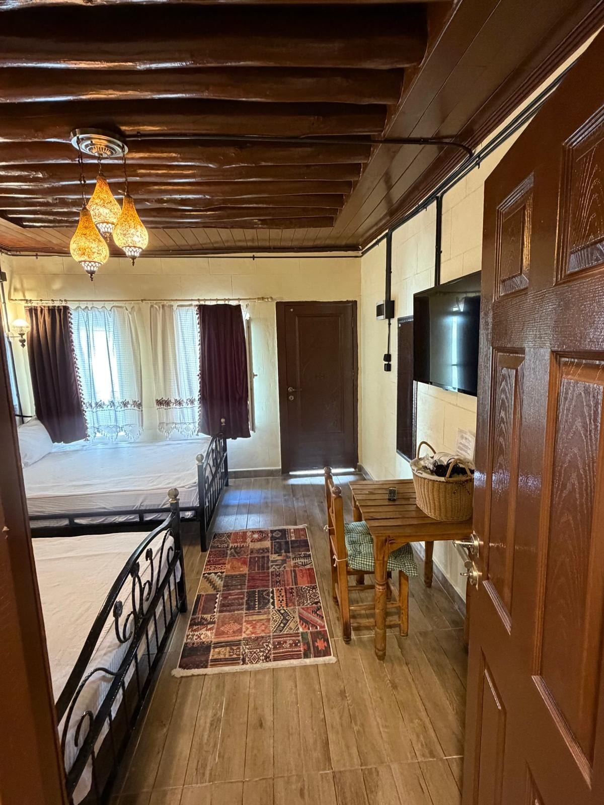 Una habitación con una cama, una mesa de comedor con sillas, un tapete estampado y un techo de madera.
