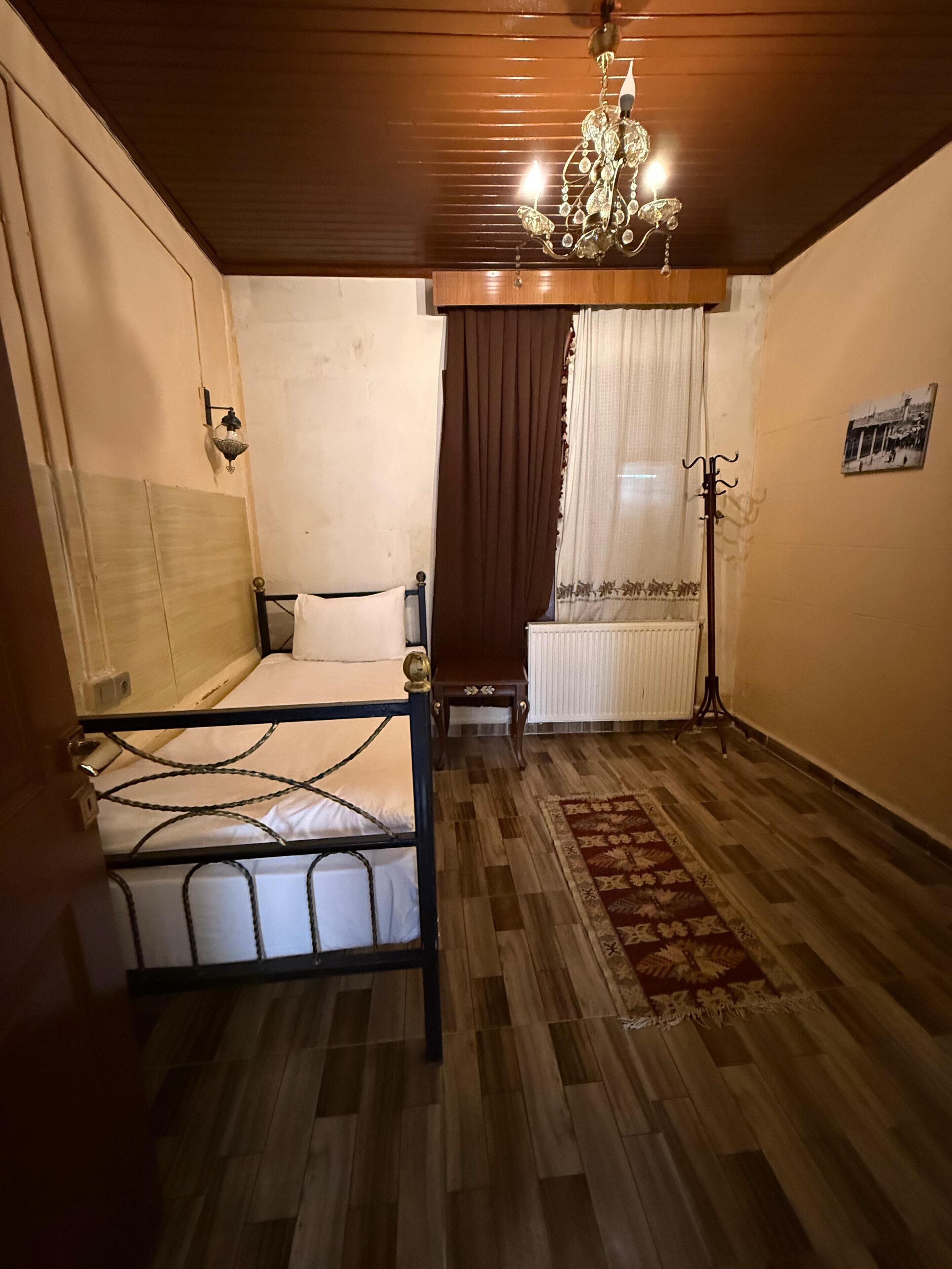 A small, cozy room with a single bed, a wooden floor, a chandelier, and a radiator.