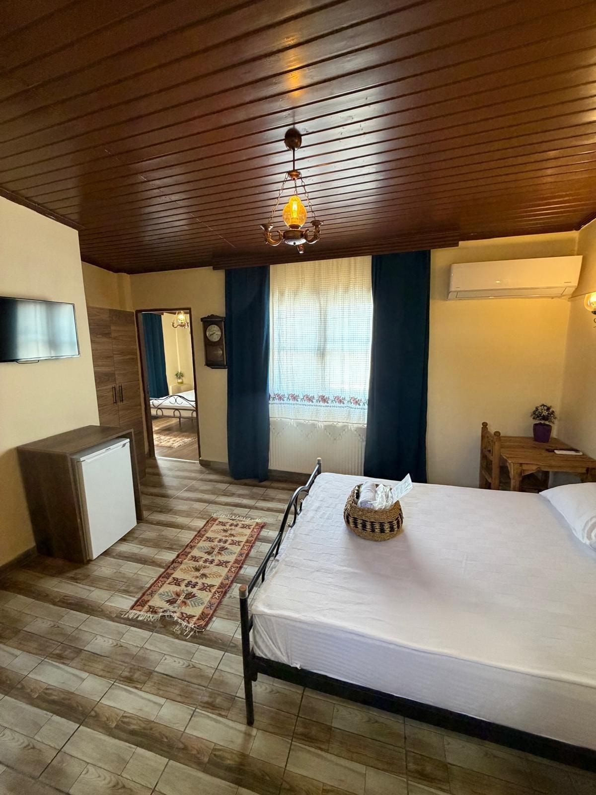 A hotel room with a bed, a desk, a television, a clock, and an air conditioning unit.