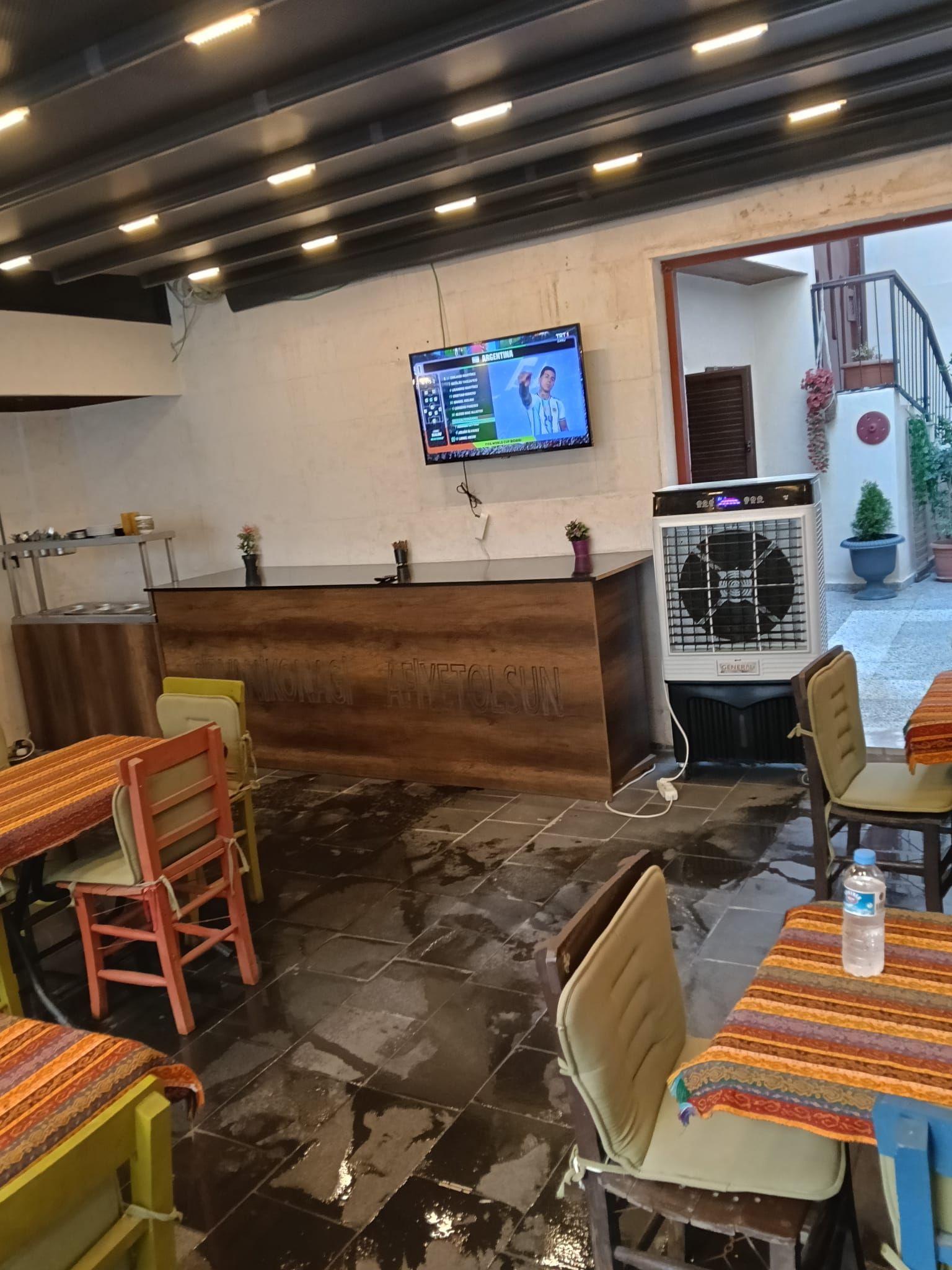 A restaurant interior with a wooden reception desk, a television mounted on the wall, and a tiled floor.