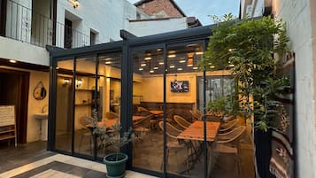 A courtyard with a glass-enclosed dining area, potted plants, and a trash bin.