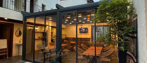 A courtyard with a glass-enclosed dining area, potted plants, and a trash bin.