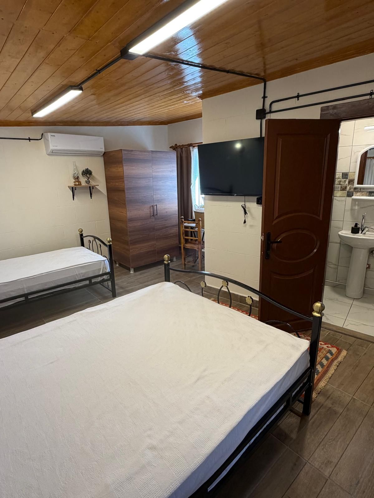 Une chambre à coucher comprenant un lit, une armoire, un téléviseur et une salle de bain avec un lavabo.