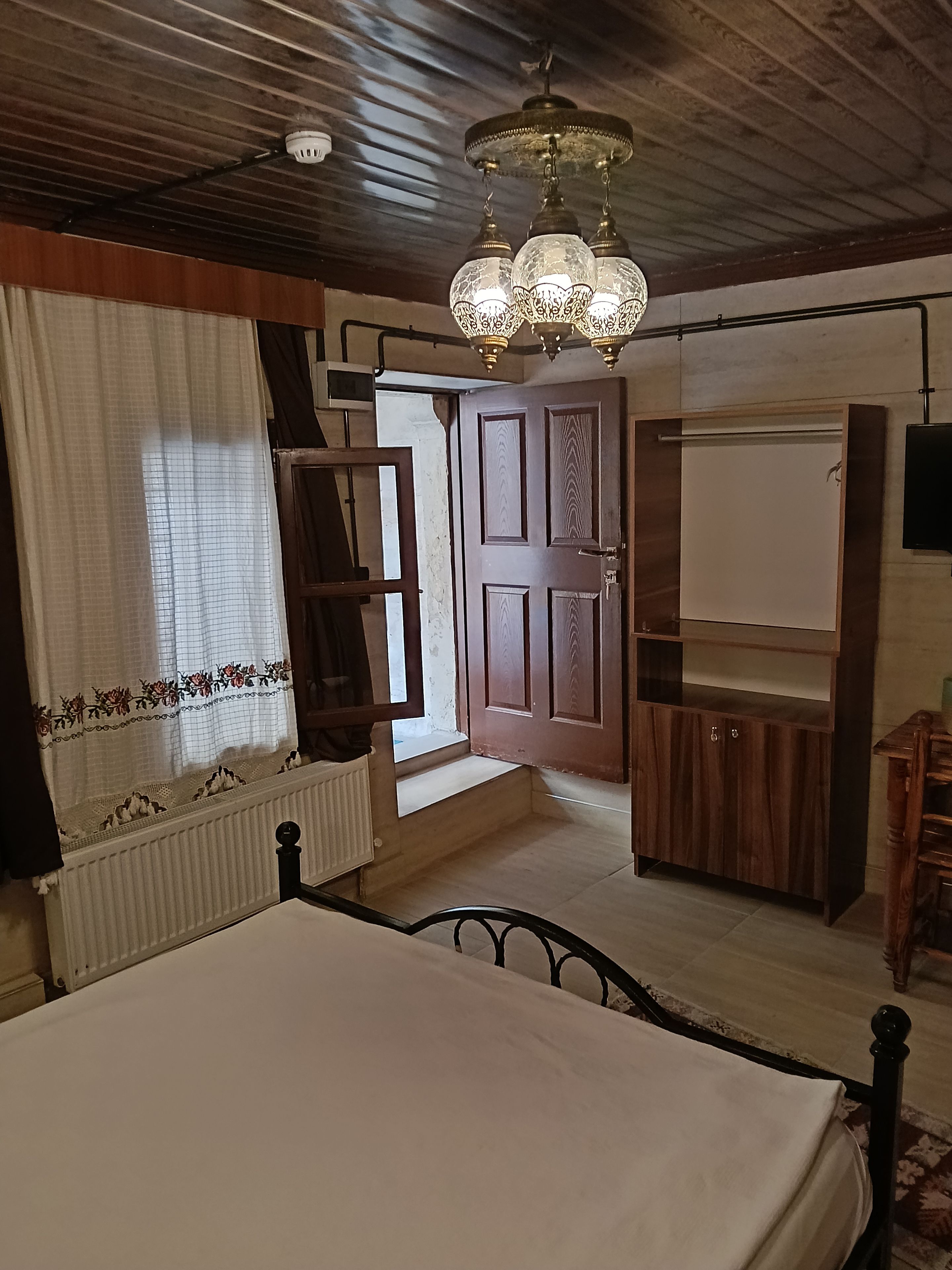 Une chambre à coucher avec un lit, une armoire en bois, un radiateur et une fenêtre avec des rideaux.