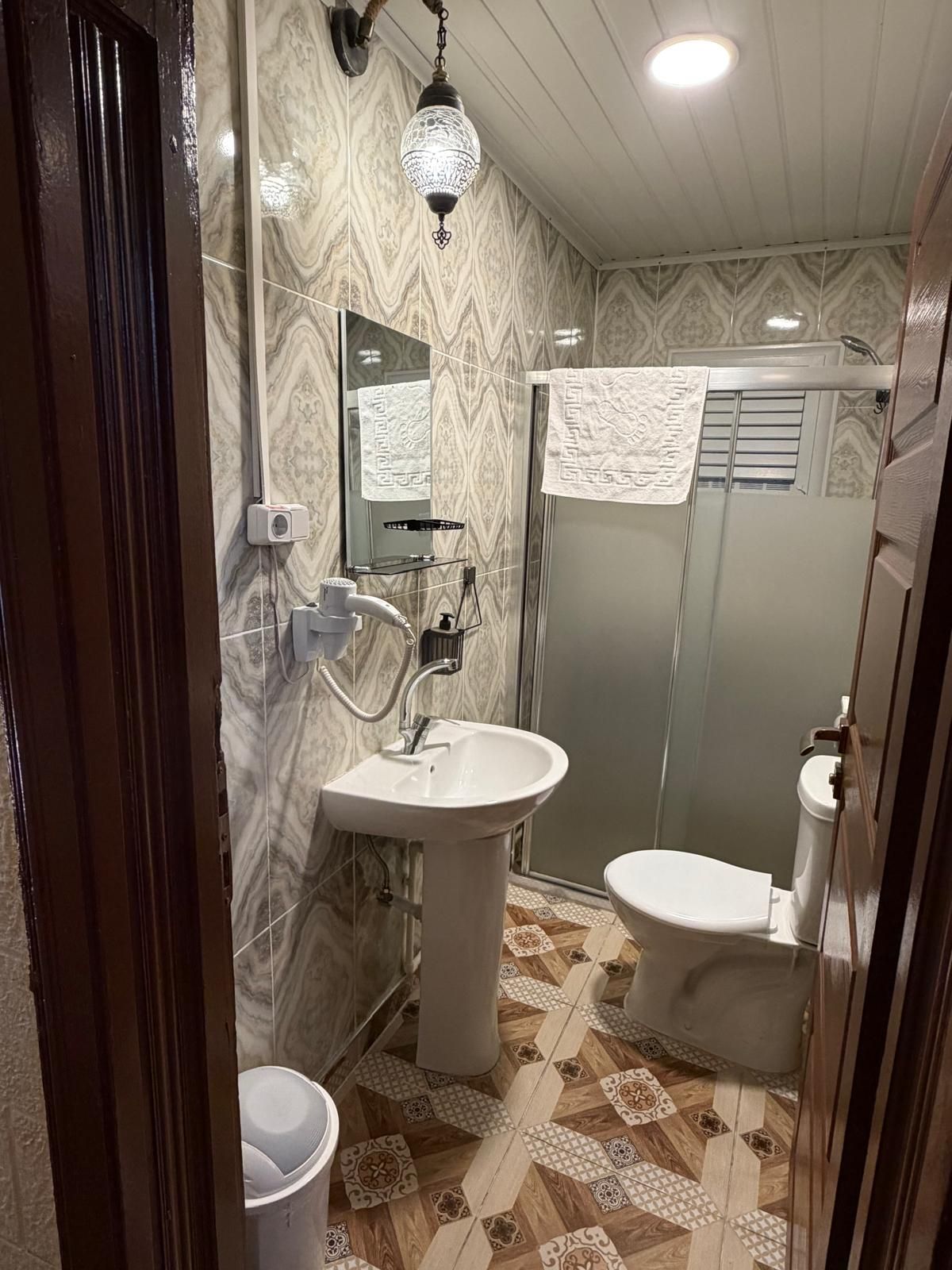 A bathroom with a pedestal sink, a toilet, a shower enclosure, and a patterned floor.