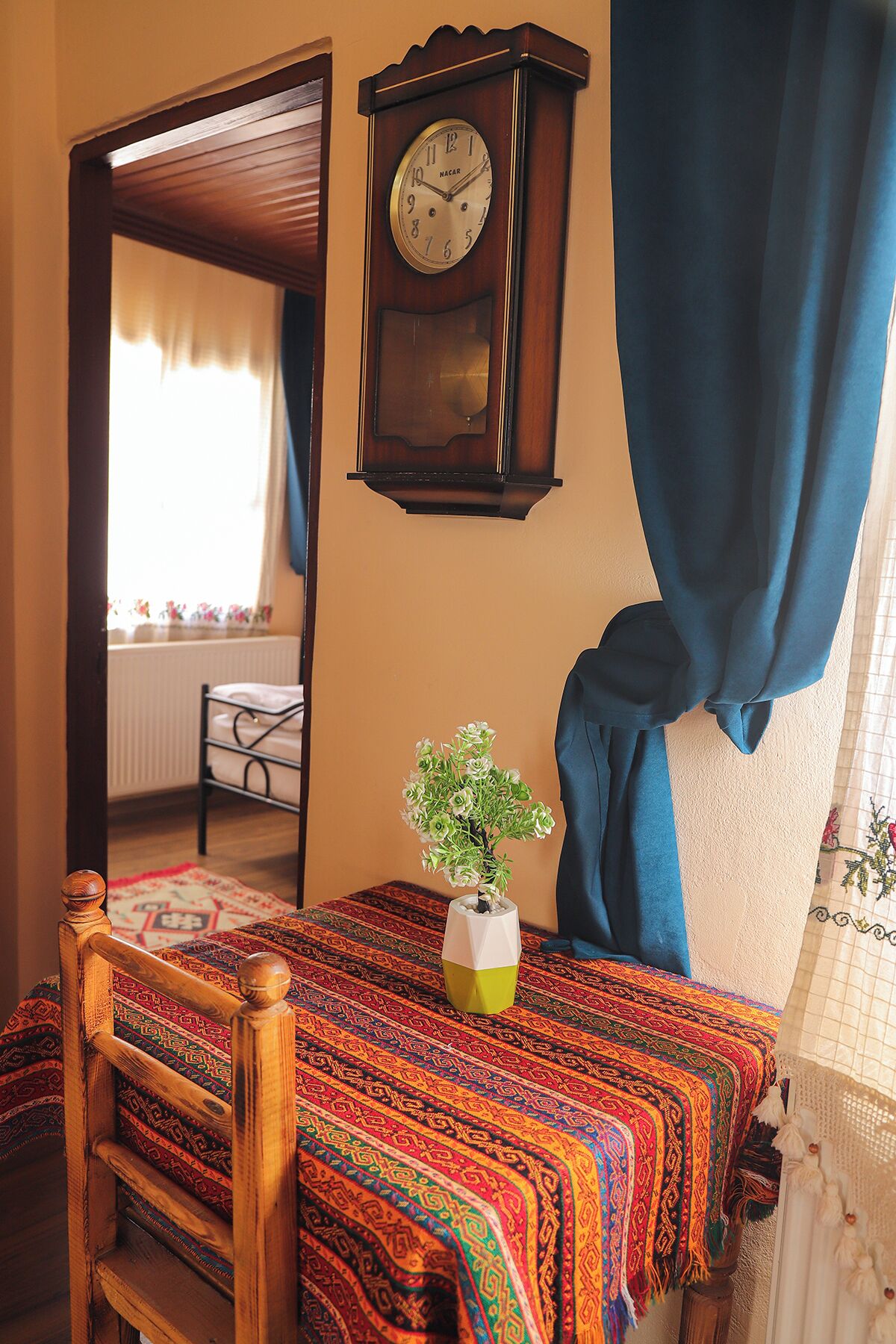 Un dormitorio con cama de madera, un reloj de pared, una ventana con cortinas y una pequeña planta en maceta.