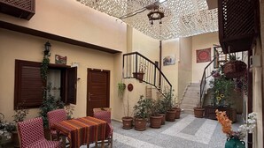 Un cortile con pavimento in piastrelle, un tavolo di legno con tovaglia decorata e diverse piante in vaso.