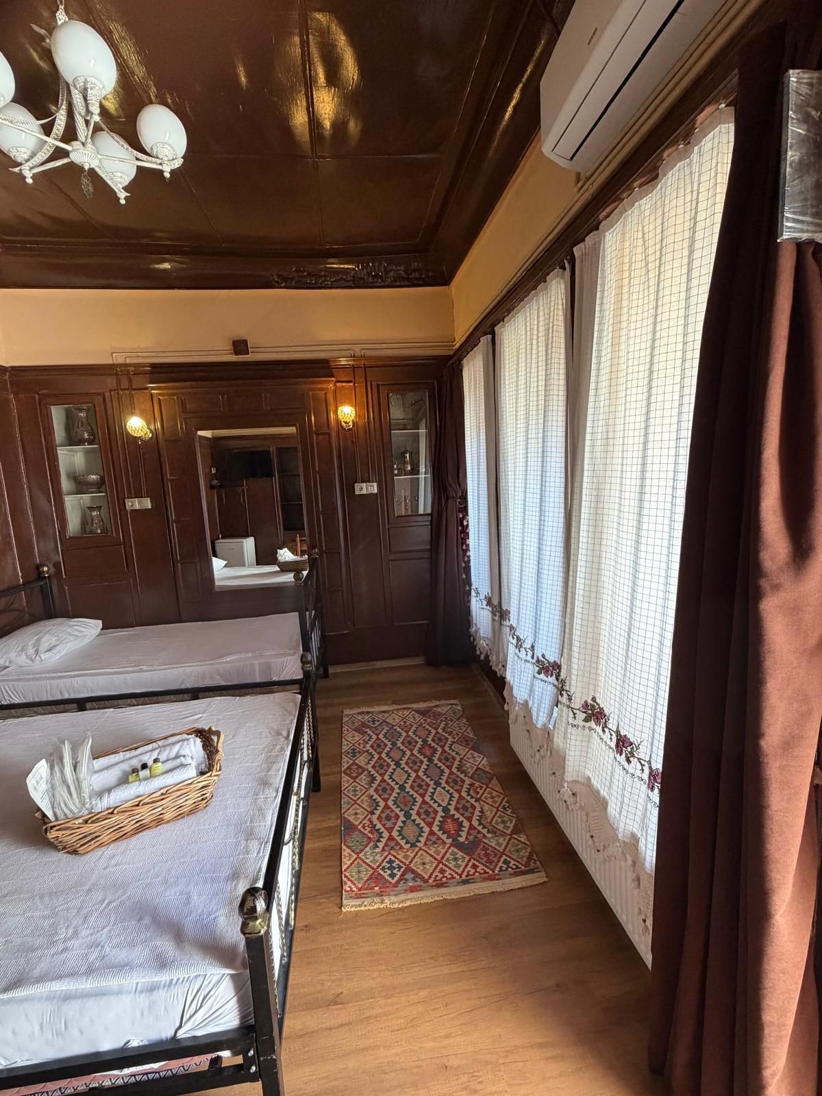 Ein Hotelzimmer mit zwei Betten, einer Kristallleuchtre, einem großen Spiegel, einem Fenster mit Vorhängen und einer Klimaanlage.