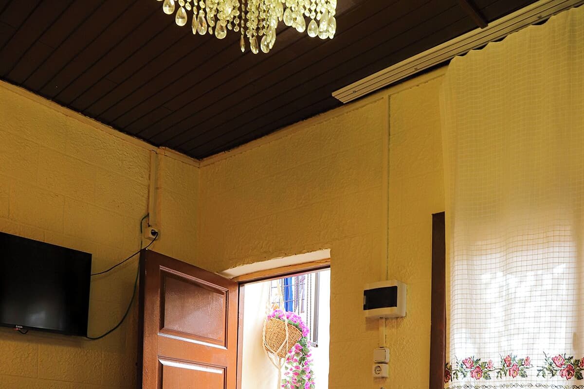 A bedroom with a bed, a wooden wardrobe, a television, and a window with a curtain.