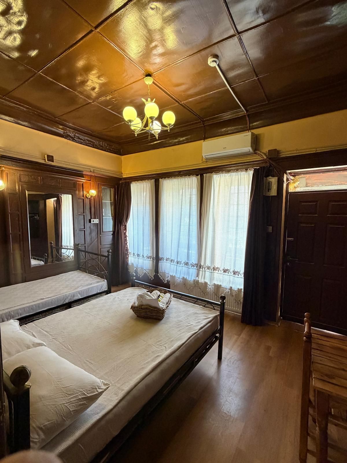 A room with two beds, a chandelier, an air conditioning unit, and a window with curtains.