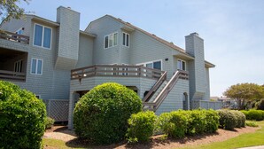 A multi-story residential building with a balcony, a staircase, and well-maintained landscaping. - Oceanside, Lighthouse Views, Community Pool, Community Amenities, 601, Our Happy Place (Corolla)