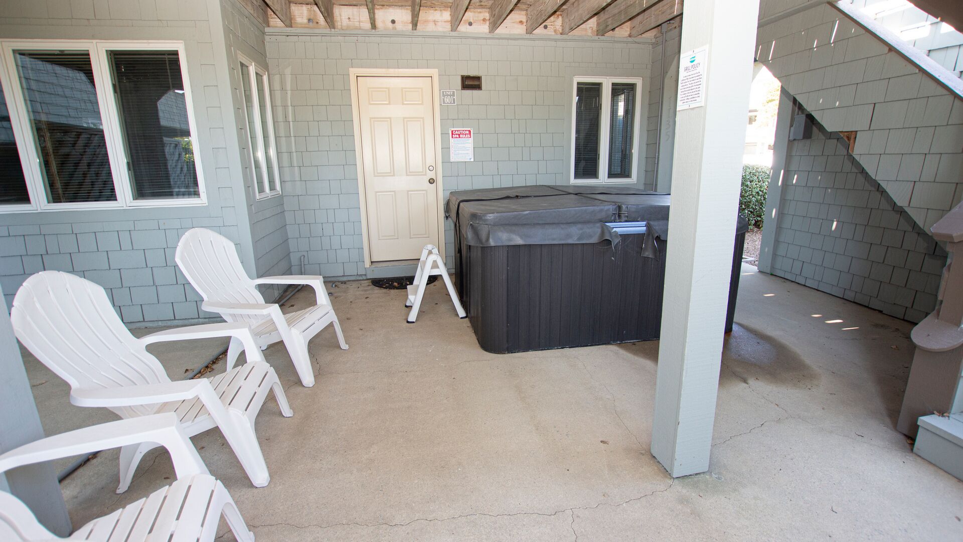 A covered outdoor area with a hot tub, white plastic chairs, and a door.