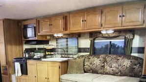 Une cuisine compacte pour camping-car, avec des placards en bois, un four à micro-ondes et une cuisinière.