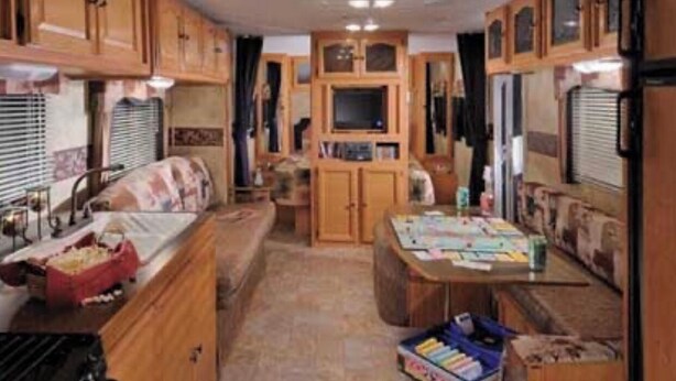 A compact RV kitchen with wooden cabinets, a sink, and a dining area. - Frontier days special, RV camper sleeps 6 (Cheyenne)