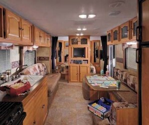 Cucina compatta per camper con mobili in legno, lavandino e zona pranzo.