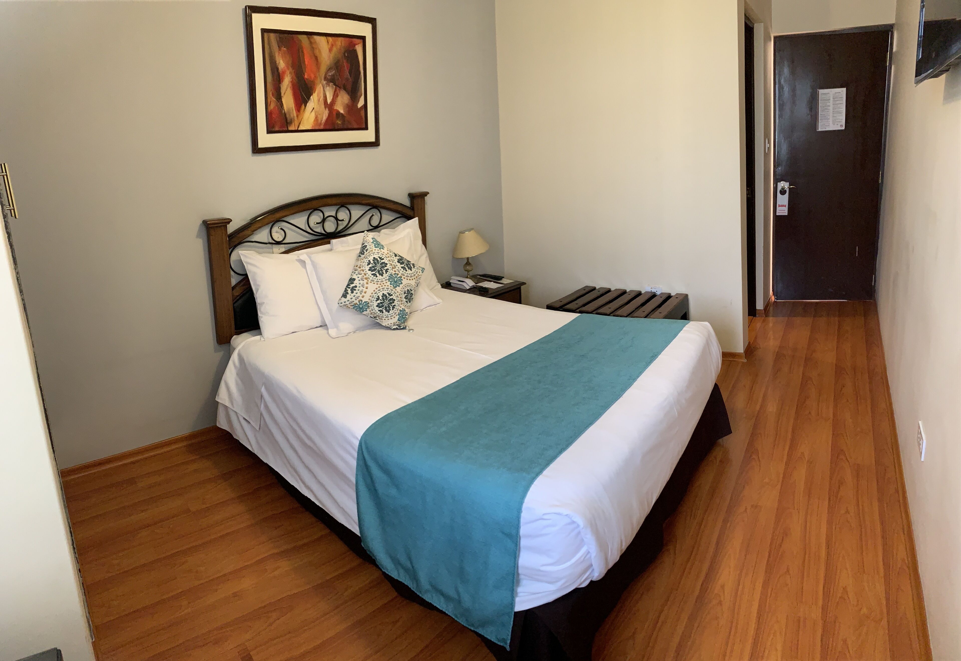 Un lit bien fait, avec une couverture turquoise, une tête de lit en bois et un seul coussin décoratif.