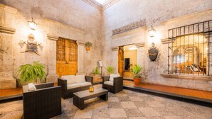 A lobby with wicker furniture, potted plants, and a stone floor.