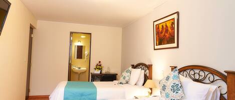 A hotel room with two beds, a bathroom with a sink, a mirror, and a framed picture on the wall.