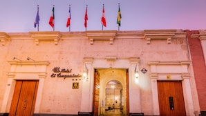 The entrance to El Conquistador Hotel with a wooden door, a sign above the door, and multiple flags on the roof.