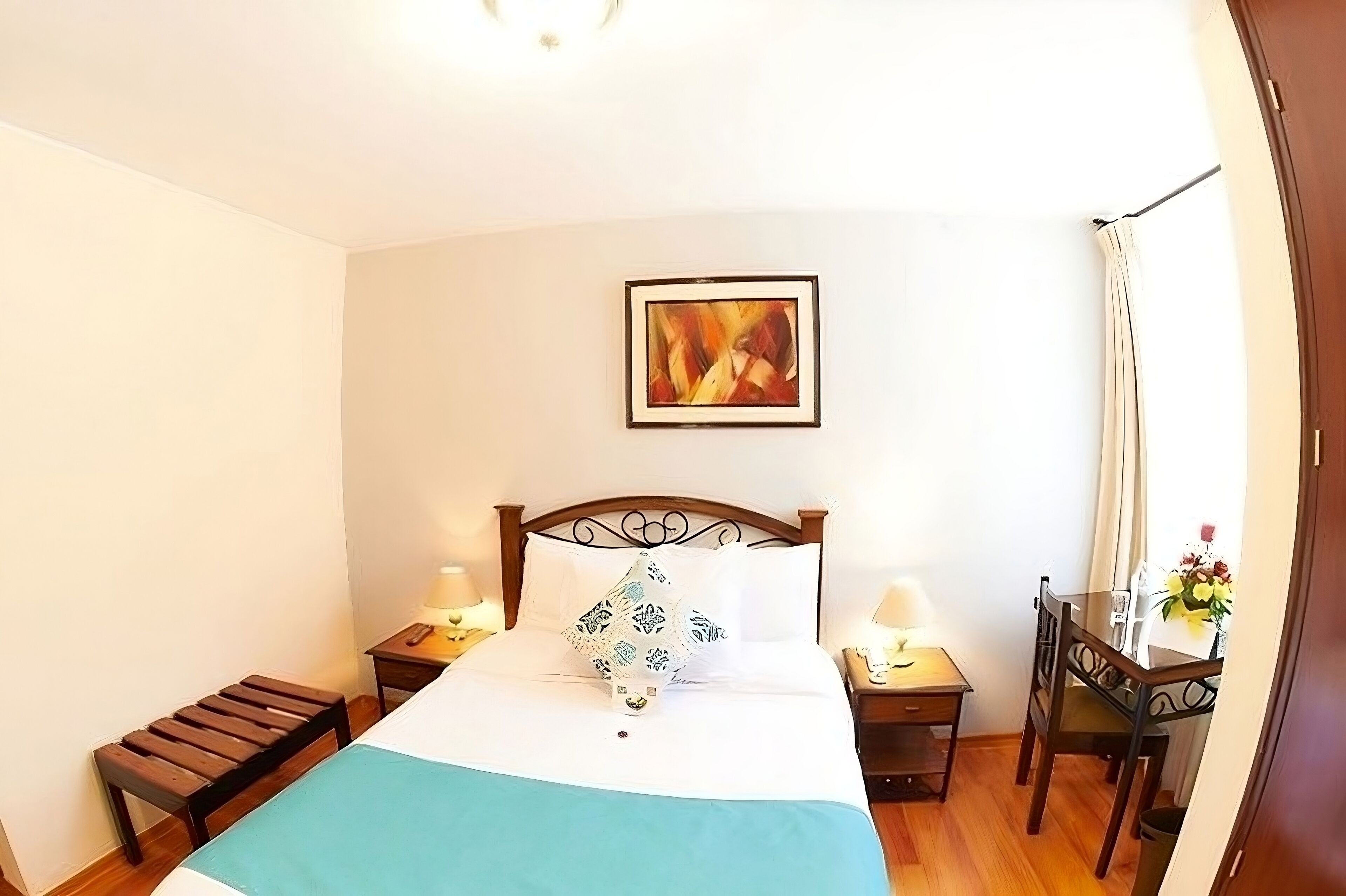 Un dormitorio ordenado con cama, mesitas de noche, una silla y un cuadro en la pared.