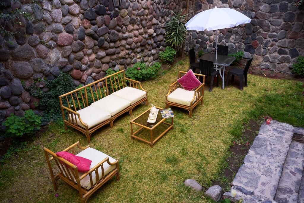 Un patio con mobiliario de mimbre, un muro de piedra y un paraguas blanco.