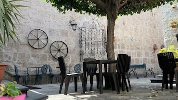 Un patio al aire libre con una mesa y sillas, un árbol que da sombra y un muro de piedra al fondo.