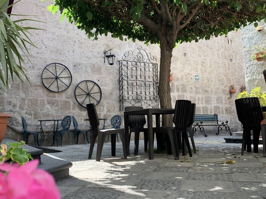 Un patio al aire libre con una mesa y sillas, un árbol que da sombra y un muro de piedra al fondo.