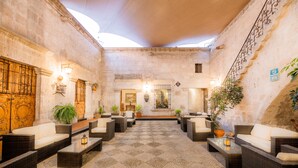 A spacious courtyard with wicker furniture and potted plants, featuring a stone floor and a high ceiling.