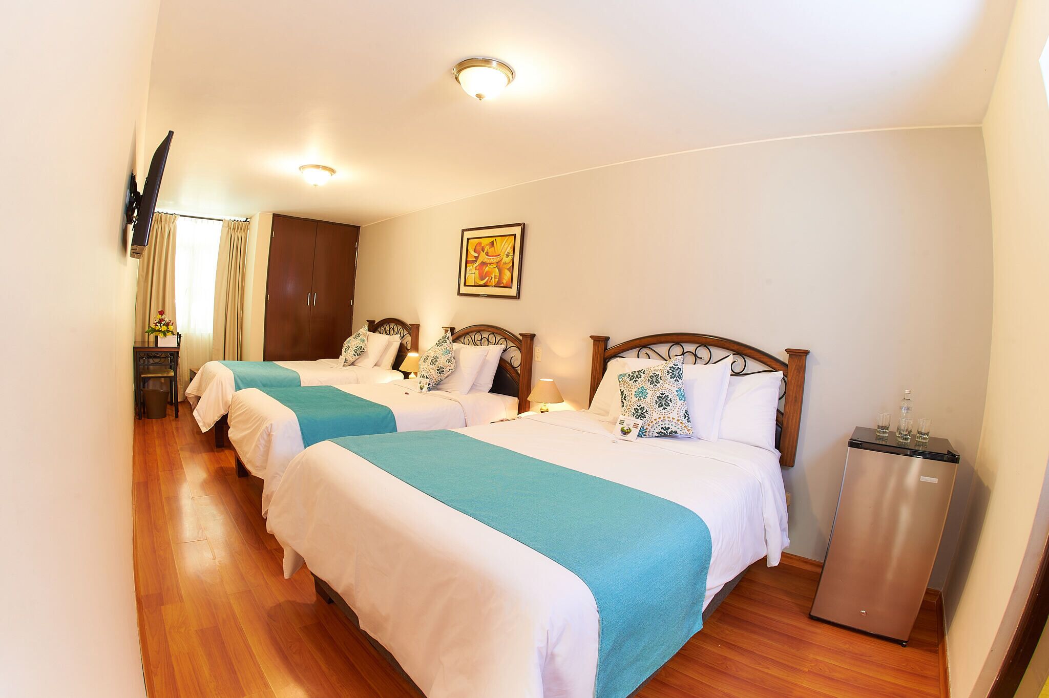 Une chambre d’hôtel avec deux lits, un plancher en bois, un téléviseur à écran plat, un réfrigérateur et un tableau au mur.