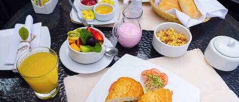 Una mesa con una variedad de alimentos para el desayuno, incluyendo un sándwich, un bol de fruta y bebidas.