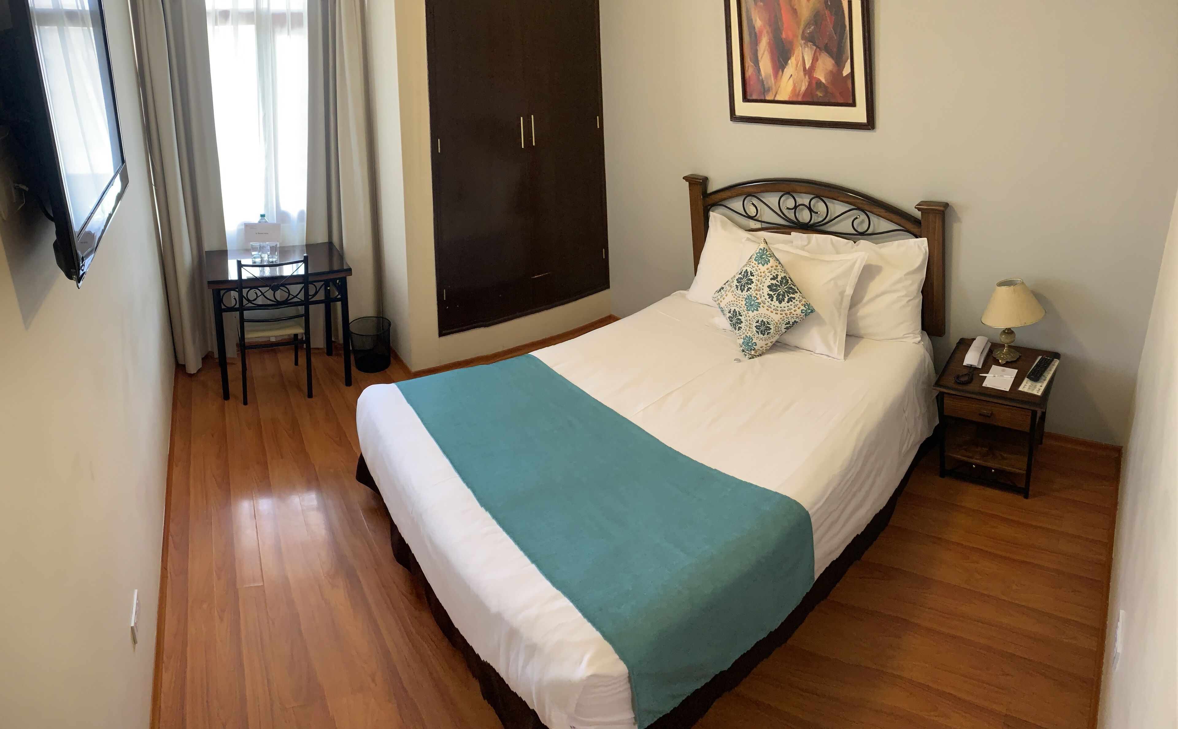 Un dormitorio ordenado con cama, mesita de noche, lámpara y un escritorio con silla.