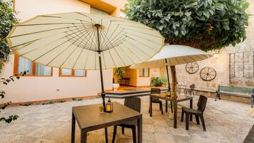 An outdoor patio with wicker furniture, two umbrellas, and a large potted plant.