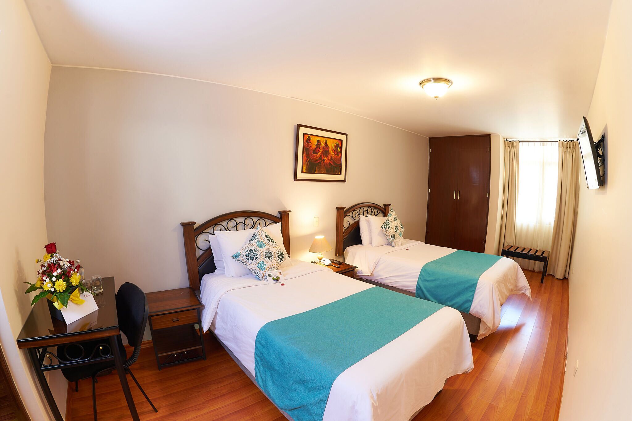 A hotel room with two beds, a desk with a chair, a desk lamp, and a painting on the wall.