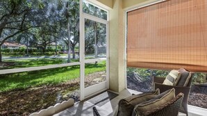 A room with a large window, a wicker chair, and a view of a landscaped garden. - Cozy Condo on Golf Course/Summer Rental/ Fort Myers  (Fort Myers)