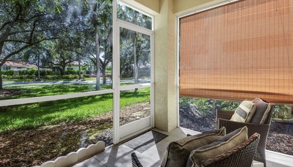 A room with a large window, a wicker chair, and a view of a landscaped garden. - Cozy Condo on Golf Course/Summer Rental/ Fort Myers  (Fort Myers)