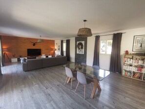 Ein modernes Wohnzimmer mit einem Glastisch, einem grauen Sofa und einem Fernseher an einer Holzwand.