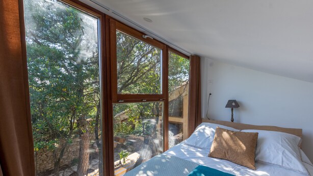A bedroom with a large window, a bed with pillows, and a lamp on the nightstand. - eco-lodge with natural swimming pool (PUECHABON)