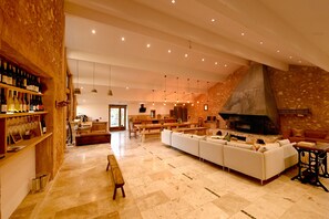 A spacious living area with a stone wall, a fireplace, and a long white sofa. - eco-lodge with natural swimming pool (PUECHABON)