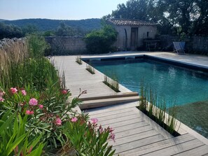 A swimming pool with a wooden deck, surrounded by greenery and a rustic building. - eco-lodge with natural swimming pool (PUECHABON)