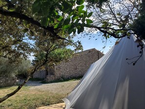 A tent set up in a grassy area with a stone wall and trees in the background. - eco-lodge with natural swimming pool (PUECHABON)