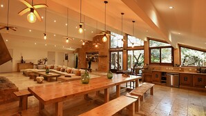 A spacious living area with a large wooden table, comfortable seating, and a kitchen with a stone accent wall. - eco-lodge with natural swimming pool (PUECHABON)