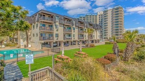 A multi-story hotel with balconies, a swimming pool, and a well-maintained lawn. - Long Bay Dunes E1 - Ocean Front 2 Bed/2 Bath Condo - Pool - 1st Floor Unit (Myrtle Beach)