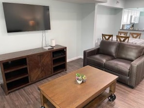 Una sala de estar con un sofá de cuero marrón, una mesa de centro de madera con una planta, un televisor montado en la pared y un mueble de madera para entretenimiento.