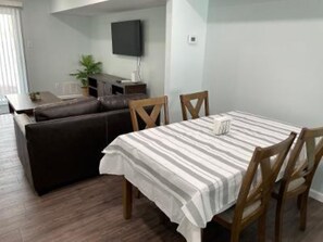 Un comedor con una mesa dispuesta para dos personas, un sofá y un televisor al fondo.