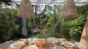 A wooden dining table set for six with white chairs, surrounded by lush greenery and a wooden fence. - Villa 3 bed 2 bath 6 pers, south facing, Golfe St Tropez, air-conditioned, free wifi (Grimaud)