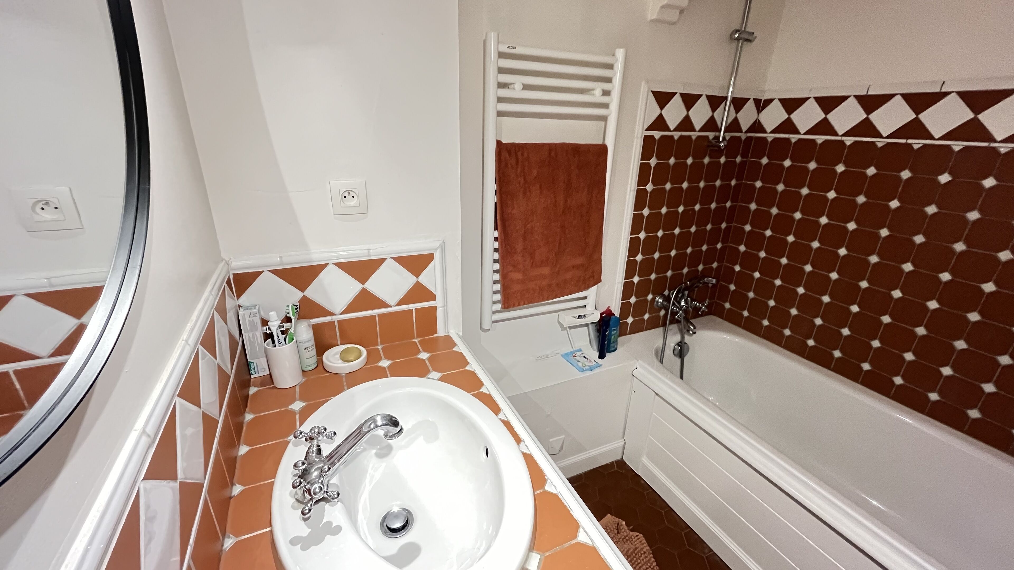 A bathroom with a white sink, a bathtub, and a shower. There is a towel hanging on a rack and toiletries on the counter.
