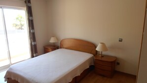 Un dormitorio con una cama, dos mesitas de noche con lámparas, una ventana con cortinas y suelo de madera.