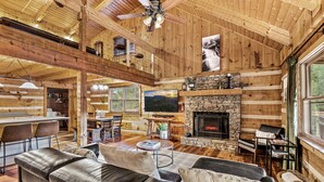 Un intérieur spacieux de chalet en bois avec une cheminée en pierre, des canapés en cuir et un coin repas.